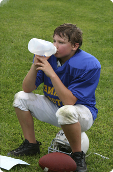 Young football player sitting down, drinking water during a break at practice