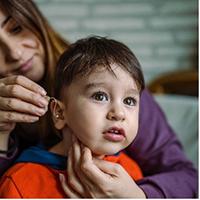 Woman installing hearing aid in young childs ear
