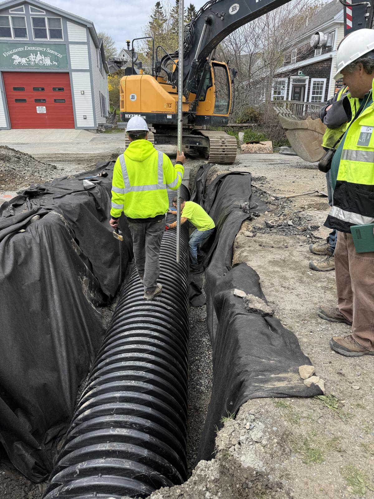 A man in a yellow jacket walking on a drainage pipe.