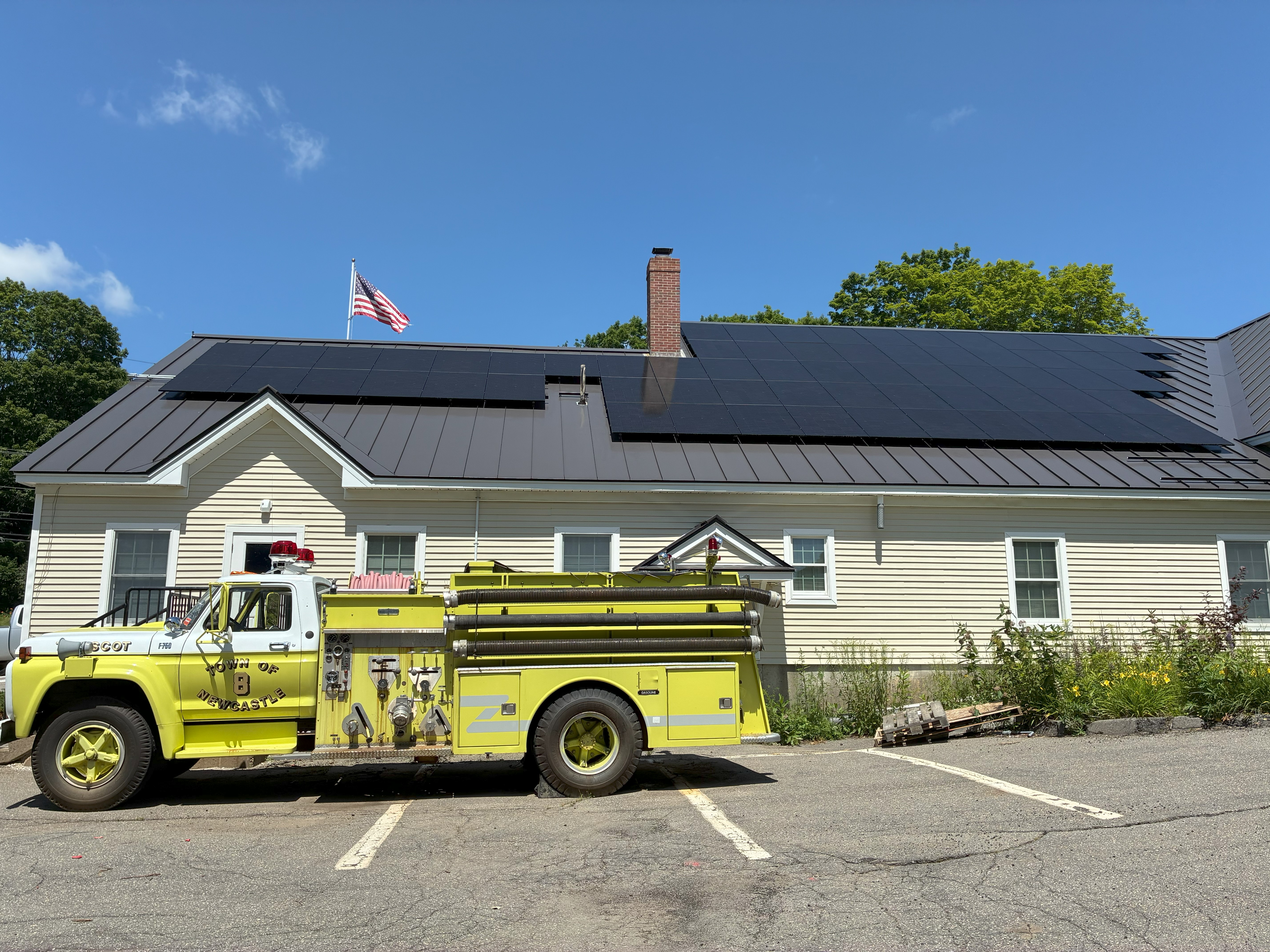 A yellow fire truck in front of a building with solar panels on the roof.