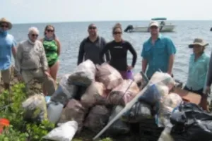 People lined up behind trash bags with the ocean behind them.