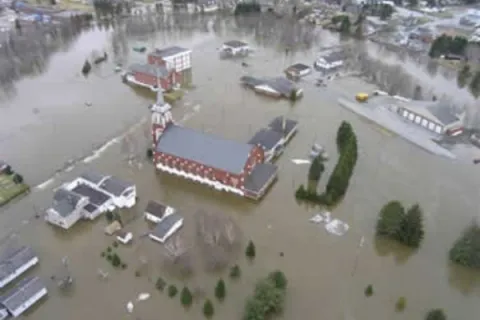 An aerial image of buildings and trees surrounded by floodwater.