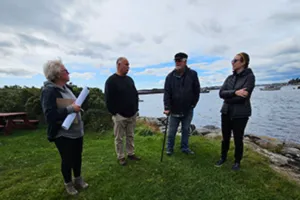 A group of four people standing on a grassy knoll with the ocean behind them.